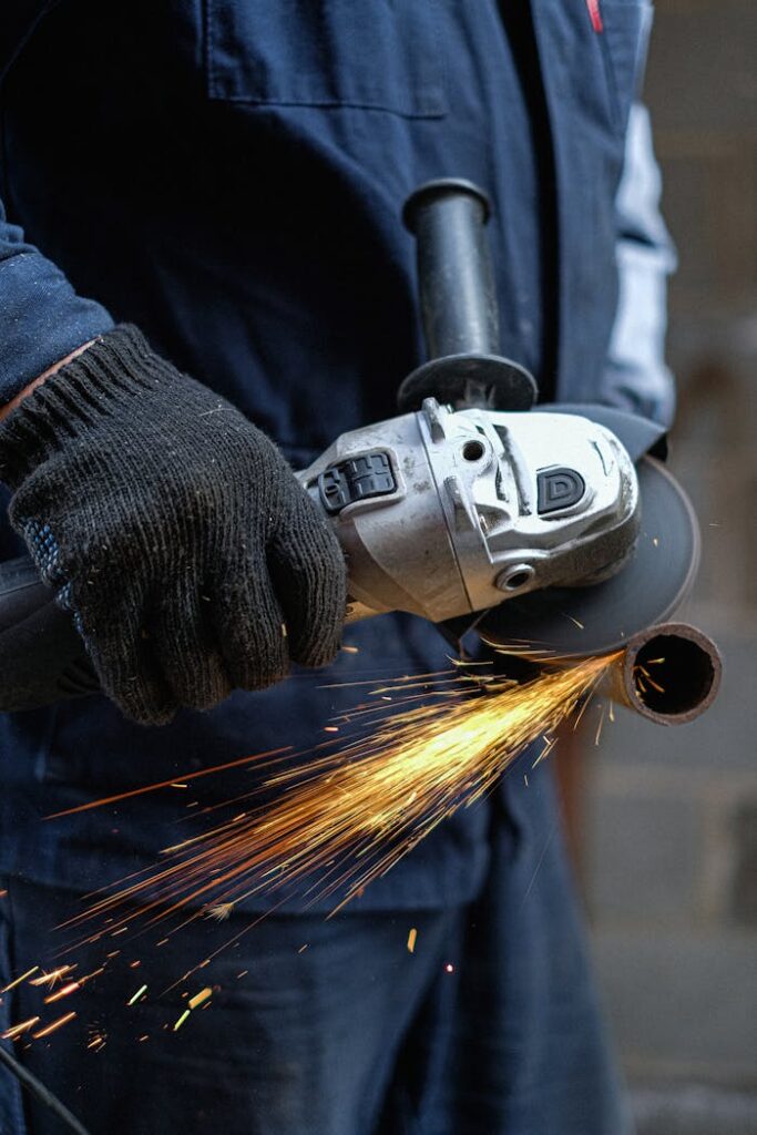 Close-up view of a man using an angle grinder, creating sparks while cutting metal in an indoor workshop.